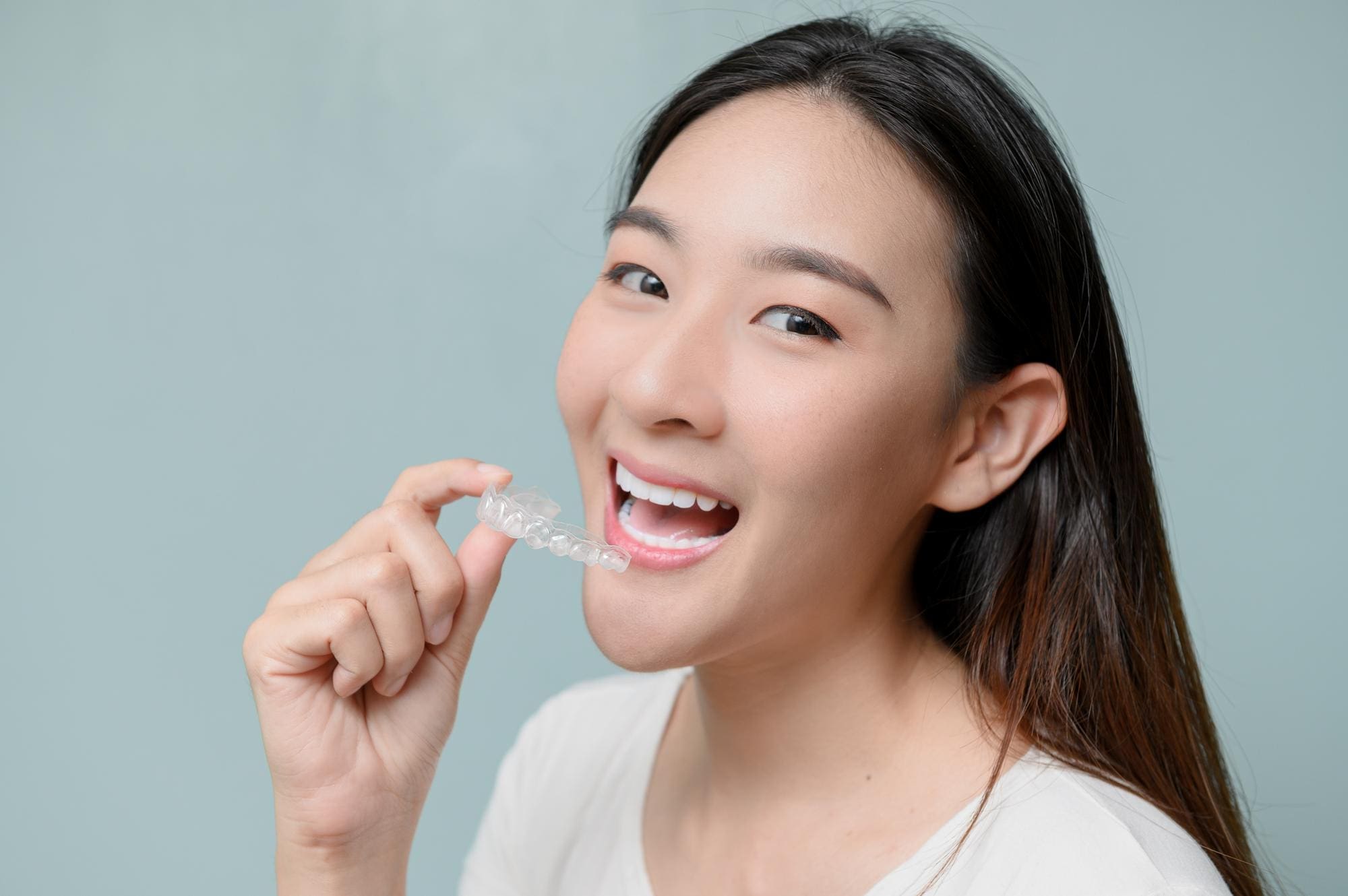 Woman holding clear aligner near mouth, showing affordable Invisalign at Carpinello Orthodontics Drexel Hill PA.