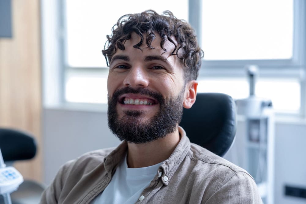 Smiling man with beard and curly hair in dental chair, showing Clear Braces at Carpinello Orthodontics in Newtown Square, PA.
