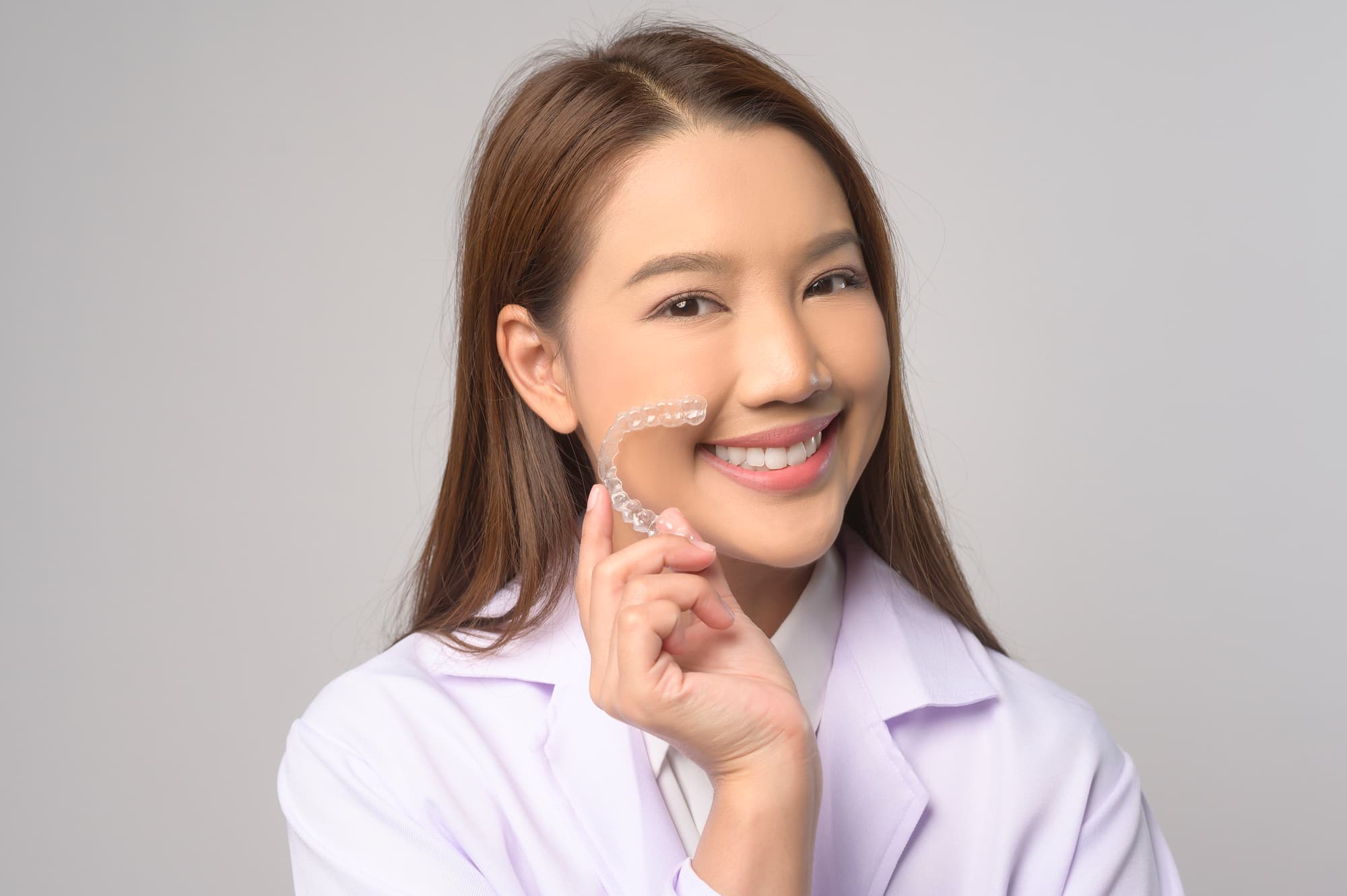 A woman in a white coat smiles, holding Invisalign® Clear Aligners at Carpinello Orthodontics in Edgmont, PA.