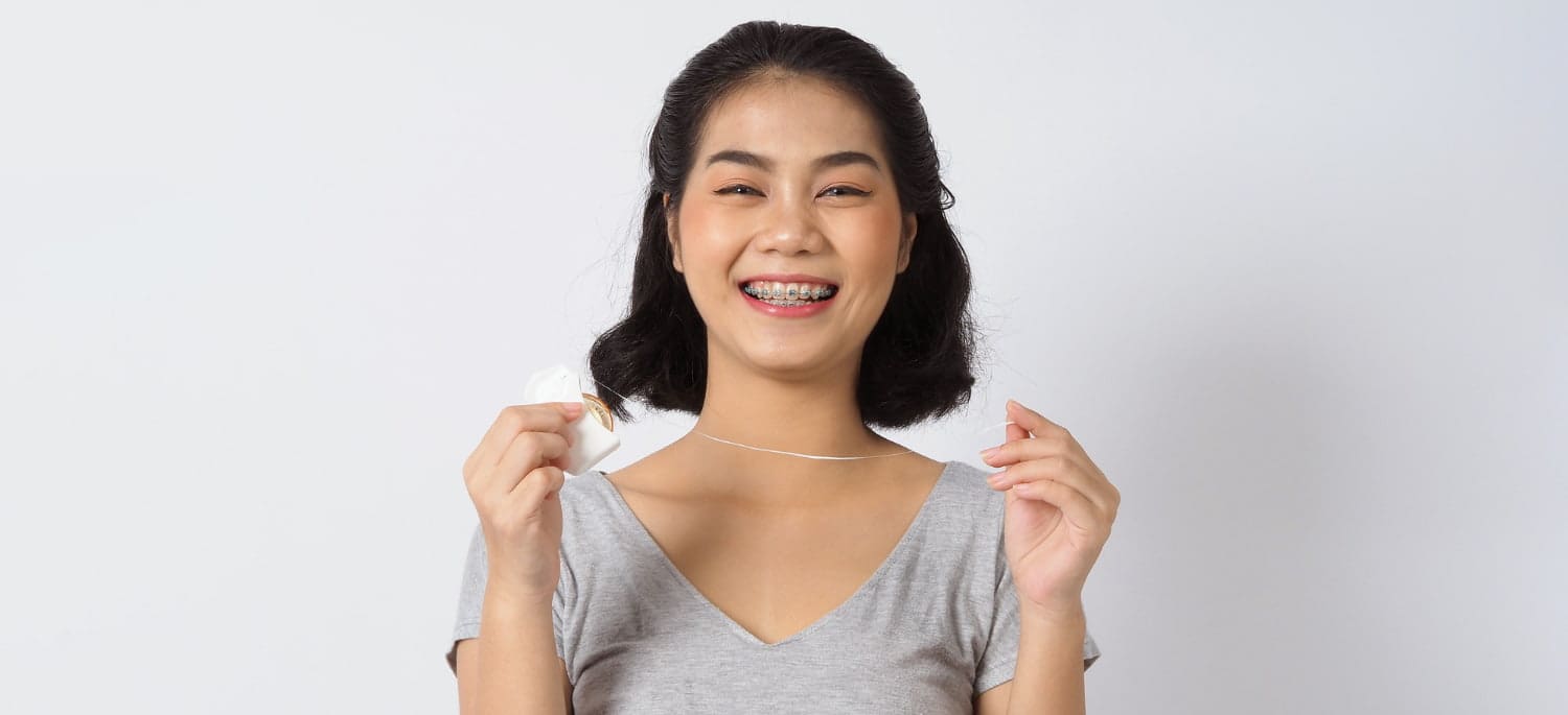 Smiling woman with metal braces demonstrates flossing, representing Carpinello Orthodontics in Edgmont, PA.