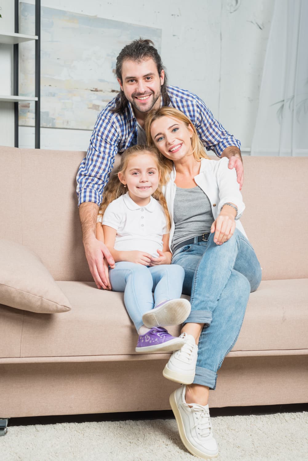 A man, woman, and girl on a beige couch smile after teeth retainer replacement at Carpinello Orthodontics in Drexel Hill, Newtown Square or Edgmont, PA.