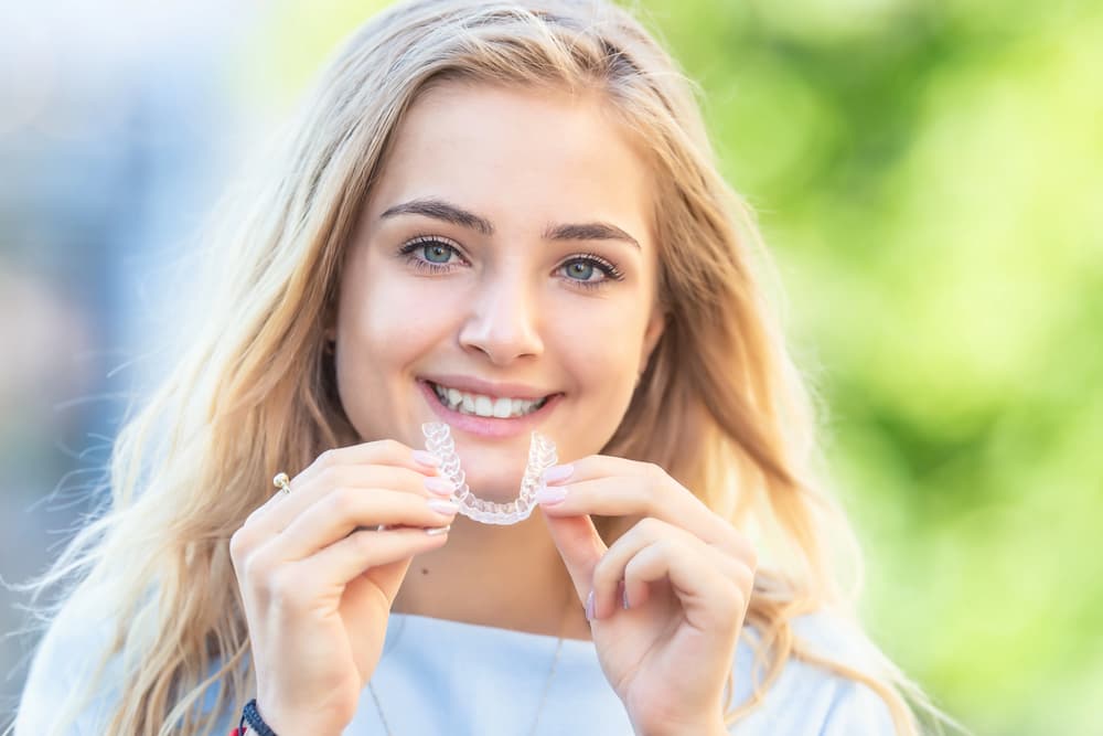 Smiling young woman with long blonde hair holds an cheap Invisalign cost at Carpinello Orthodontics in Drexel Hill, Newtown Square or Edgmont, PA - Can Invisalign Fix Overbite in Drexel Hill, Newtown Square, and Edgmont, PA
